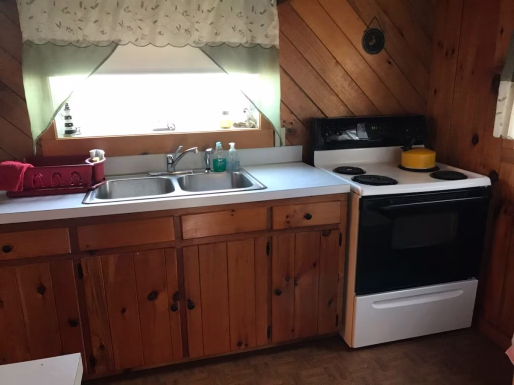 Kitchen with sink, counter, dish rack, stove, and kettle.